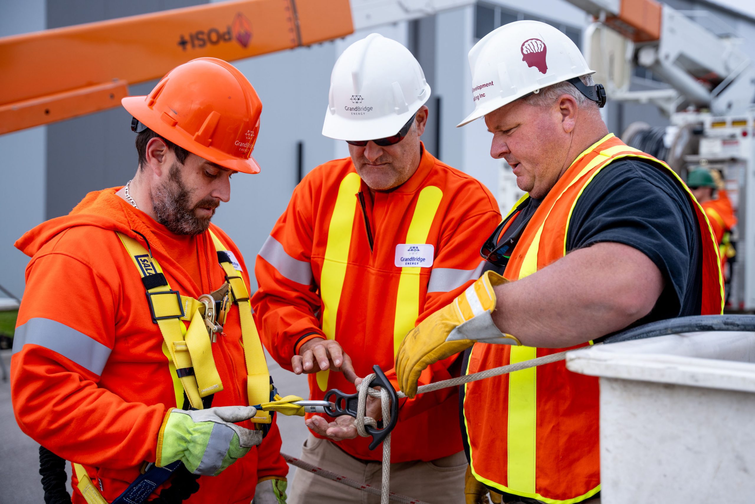 Three utility workers in safety gear inspect and adjust equipment near a bucket truck at a work site.