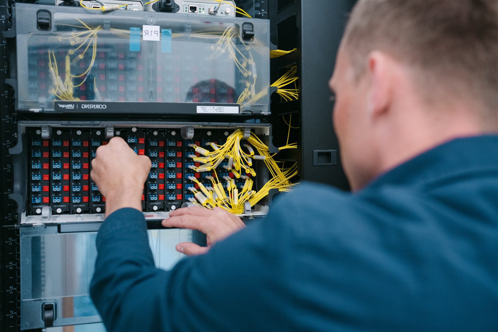 Person working on a server rack, connecting yellow network cables to multiple ports in a data center.