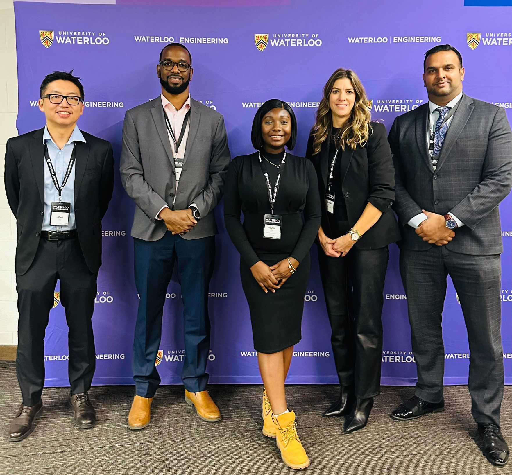 Five people in business attire stand in front of a University of Waterloo Engineering backdrop, posing for a group photo.