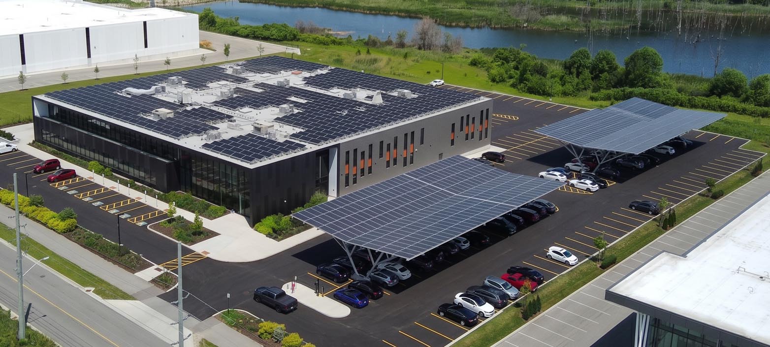 Aerial view of a commercial building and parking lot with solar panels on the roof and over parking spaces.